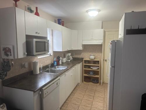 a kitchen with white cabinets and a sink and a refrigerator at Clean and Quiet 2 bdr 2 bthr private entrance entire guests suite near Coquitlam Center mall and skytrain in Coquitlam
