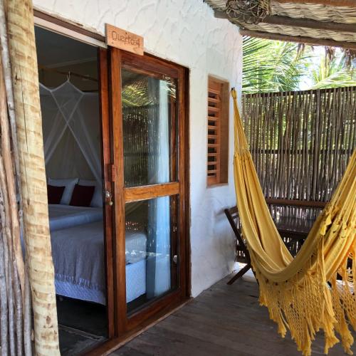 a hammock on the porch of a room with a bed at Pousada Maré Cheia in Itarema