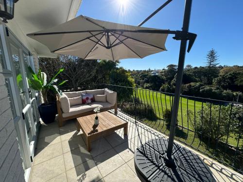 a patio with an umbrella and a couch and a table at Waiake Beach Apartments in Auckland