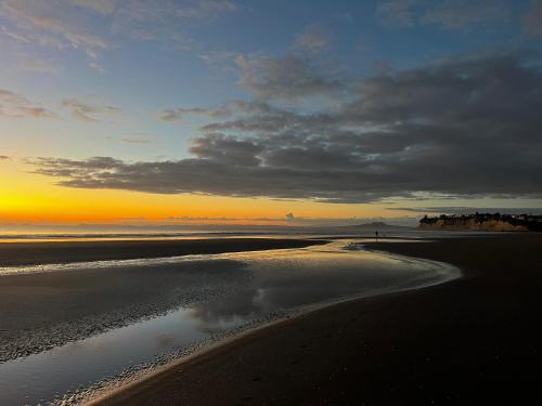 a view of a beach with the sunset in the background at Waiake Beach Apartments in Auckland
