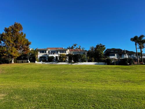 a large field of grass with a house in the background at Waiake Beach Apartments in Auckland