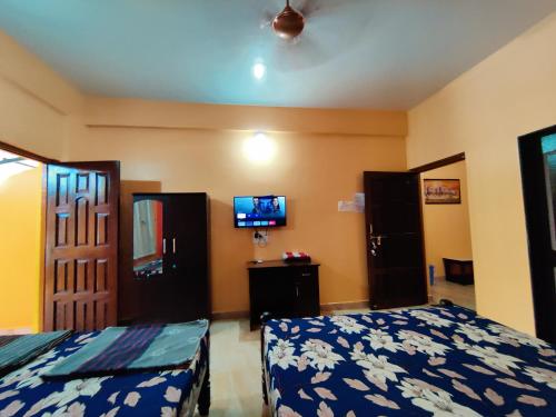 a bedroom with two beds and a tv on the wall at Sai Guru Guest House in Anjuna