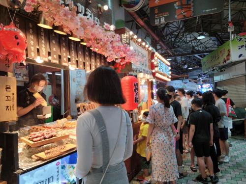 un grupo de personas caminando por un mercado con comida en Jeju Vision House en Jeju