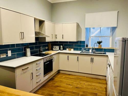 a kitchen with white cabinets and a wooden floor at Beautiful spacious apartment in town centre in Oban
