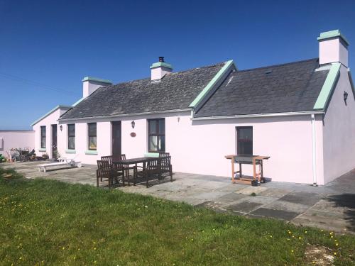 a white house with a picnic table and benches at Little Reds Seaview Cottage in Liscannor