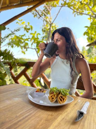 a woman sitting at a table drinking from a cup at La Veranda Hotel & Restaurant in Minca