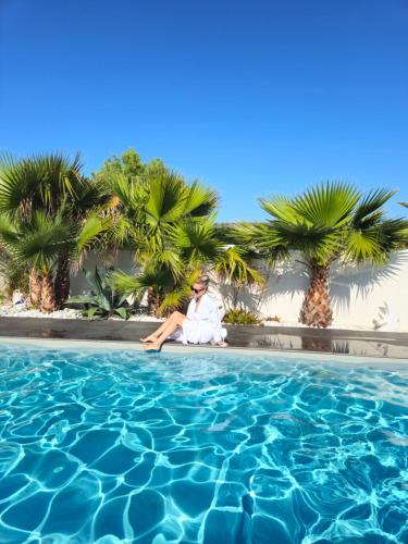 una persona sentada junto a una piscina con palmeras en Hôtel Ancre Marine & Spa Thalgo ***, en Noirmoutier-en-l'Île
