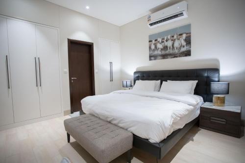 a white bedroom with a large bed and a stool at The Hawana Pearl لؤلؤة هوانا in Salalah