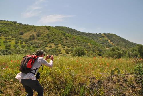 a man with a backpack taking a picture of a hill at Ferme Dar Aicha green Bellouta in Bellouta