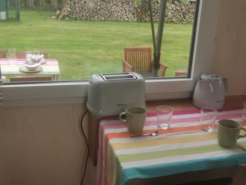 a table with a toaster and cups on a table with a window at Tiny du Verger de la Pommeraye in Morgny-la-Pommeraye