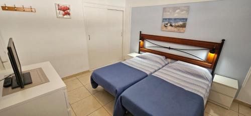 een slaapkamer met een blauw bed en een televisie bij Los Geranios in Adeje