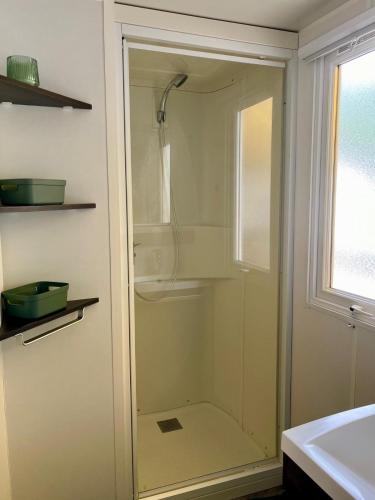 La salle de bains est pourvue d'une douche en verre et d'un lavabo. dans l'établissement Mobil Home Vias plage La Carabasse terrasse fermée hors saison, à Vias