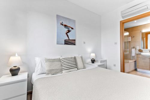 a white bedroom with a bed and a painting on the wall at Apartment Theia with sea and sunset views, the Resort in Aphrodite Hills in Kouklia