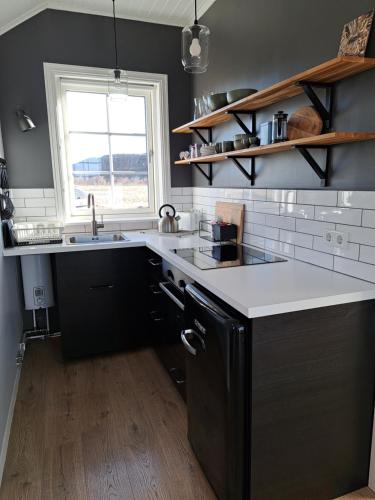 eine Küche mit schwarzen Schränken, einem Waschbecken und einem Fenster in der Unterkunft Gíslaholt in Borgarnes