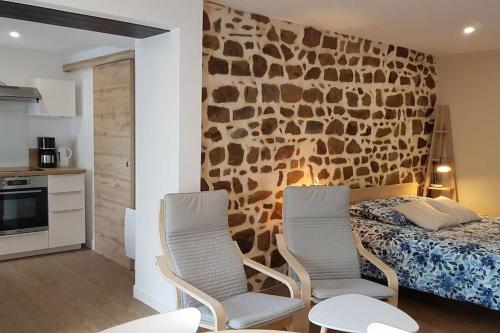 deux chaises et un lit dans une pièce avec un mur en pierre dans l'établissement Studio chaleureux 5 mns chaine des Puys, à Saint-Genès-Champanelle