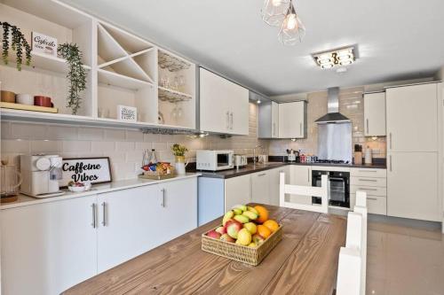 a kitchen with white cabinets and a basket of fruit on a table at Radiant Retreat Ideal for LegoLand, Windsor, & LHR in Slough