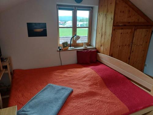 a bedroom with a large orange bed with a window at Apartment Moosblick zwischen Bergen und See in Benediktbeuern