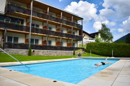 a person swimming in a swimming pool in front of a building at Kreativ Hotel Landhaus Schweigl in Ultimo
