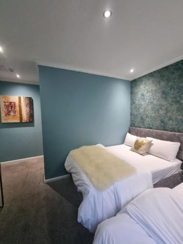 a bedroom with two beds and a blue wall at An Exquisite Deluxe Room in a Hotel - Free Parking - with access to Resturant - Shisha Bar- Wine Bar in Roundhay
