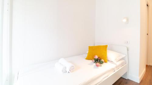 a white bed with a yellow pillow and flowers on it at Ceramic Rooms in Oristano