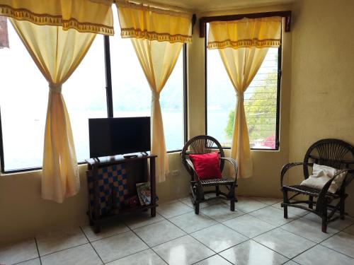 a room with two chairs and a tv and windows at Hotel Restaurante La Villa de los Dioses in San Antonio Palopó