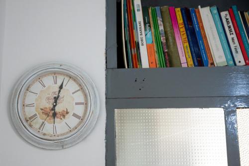 a clock on a wall next to a shelf with books at Nano Apartment in Prizren