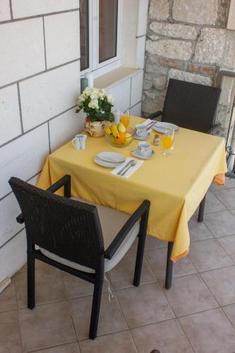 a table with a yellow table cloth and fruit on it at Divna Apartments and Rooms in Račišće