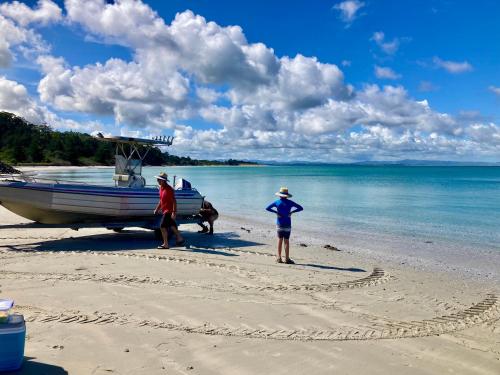 two people standing on a beach with a boat at Far North Panorama in Kaingaroa