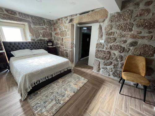 - une chambre dotée d'un mur en pierre avec un lit et une chaise dans l'établissement Casa do Compasso, à Farminhão