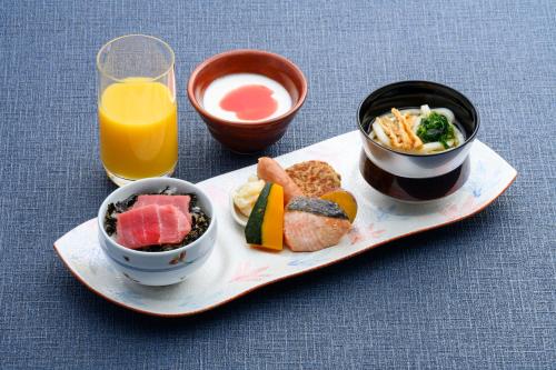a plate of food with bowls of food and a glass of orange juice at Hotel Monterey Okinawa Spa & Resort in Onna