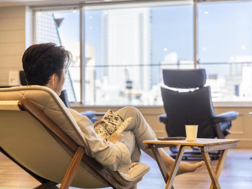 a man sitting in a chair looking out the window at Hotel Wing International Shizuoka in Shizuoka