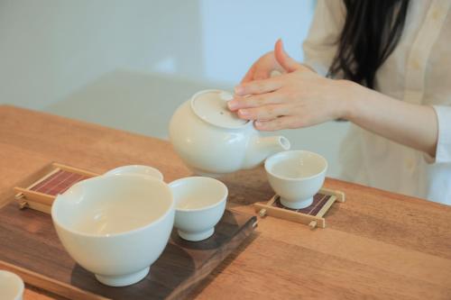 Eine Frau, die eine Teekanne mit vier Tassen auf dem Tisch hält. in der Unterkunft Aank Hotel Incheon Wolgot in Siheung