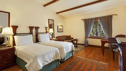 a bedroom with a bed and a desk and a window at The Oberoi Cecil in Shimla