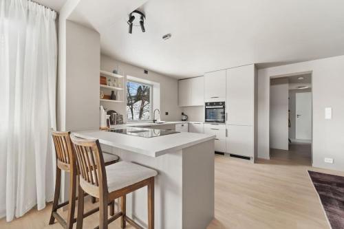a kitchen with white cabinets and a counter with chairs at Stor og moderne leilighet in Tromsø