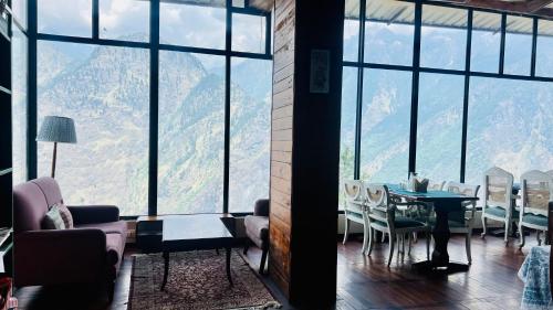 a living room with a table and chairs and windows at Faraway Cottages, Auli in Joshīmath
