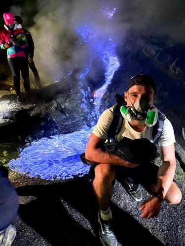 a man with a gas mask sitting on the ground with smoke at Green ijen homestay and tour in Banyuwangi