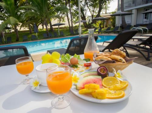 a plate of fruit and juice on a table next to a pool at Hotel Exsel Alamanda in Saint-Gilles les Bains