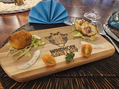 a wooden cutting board with a sandwich and vegetables on it at Windhoek Game Camp in Lafrenz Township