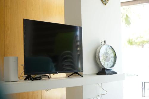 TV de pantalla plana en un estante con reloj en Searenity Seafront house - 50m from the beach, en Lárnaca