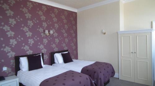 two beds in a room with purple wallpaper at The North Euston Hotel in Fleetwood