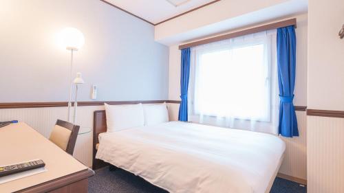 a bedroom with a bed and a window with blue curtains at Toyoko Inn Shin-Osaka-eki Higashi-guchi in Osaka