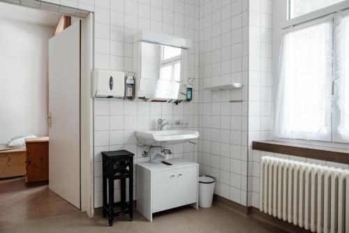 Baño blanco con lavabo y espejo en Gruppenhaus Lindenhof Churwalden, en Churwalden