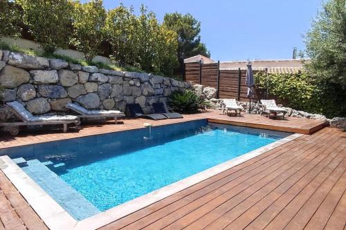 une piscine avec une terrasse en bois et un mur en pierre dans l'établissement VILLA MODERNE PISCINE JACUZZi, à Nice