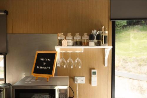 a counter with wine glasses and a sign on a microwave at Tranquility Tiny House by Tiny Away in Owaka