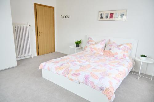 a white bedroom with a bed with a colorful comforter at Zimmervermietung Jäger in Bregenz