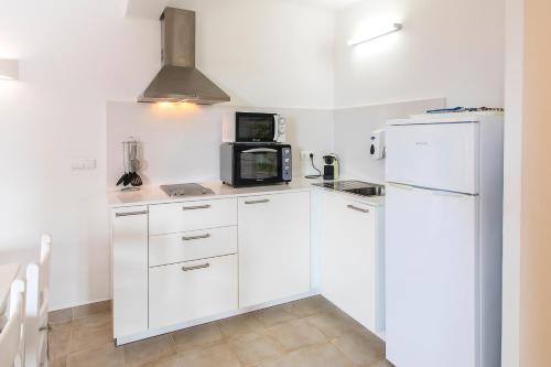 a white kitchen with a refrigerator and a microwave at Ca Sa Vilda in Es Pujols