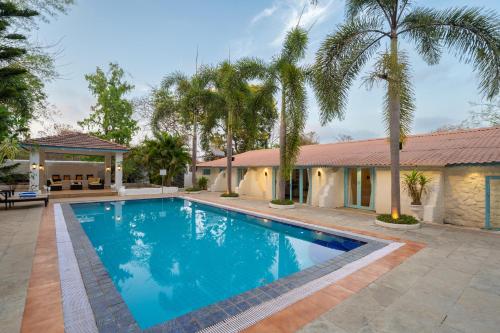 a swimming pool in front of a house with palm trees at LohonoStays Villa Santorini in Alibag