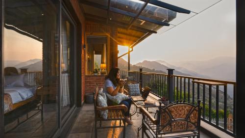 a woman sitting in a chair on a balcony at SaffronStays Aruunoday - 4BR with Theatre, Deck & Bonfire in Bhīm Tāl