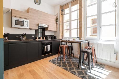une cuisine avec des placards noirs et une table avec des tabourets dans l'établissement GuestReady - Bohemian and Chic Studio Vieux Lyon, à Lyon