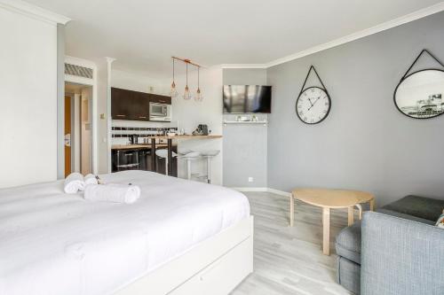 une chambre blanche avec un lit, une table et une horloge dans l'établissement Joli studio à Courbevoie - La Defense, à Courbevoie